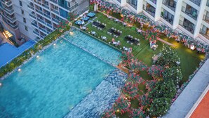 Vista aérea de um hotel com uma piscina retangular grande, áreas de estar ao ar livre e paisagismo exuberante.