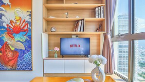 Quarto moderno com estante de madeira, televisão de tela plana, um vaso com flores e uma grande janela com vista para a cidade.