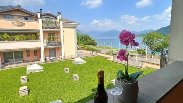 A balcony with a view of a building, a grassy area, and a body of water. - PROMENADE Luxury View (Sarnico)