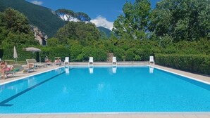 A rectangular swimming pool with clear blue water, surrounded by a tiled deck. There are lounge chairs and umbrellas along the poolside. - PROMENADE Luxury View (Sarnico)