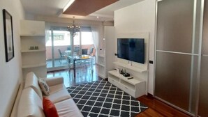 A modern living room with a sofa, TV, and a glass door leading to a dining area. - PROMENADE Luxury View (Sarnico)