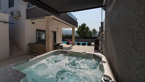 A hot tub with a stone wall backdrop, a covered outdoor seating area, and a view of mountains in the distance. - Nice home in Pridraga (Pridraga)