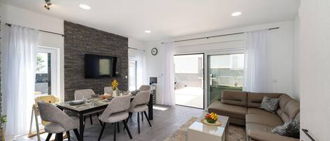 A modern living room with a dining area, a stone accent wall, a flat-screen TV, and a balcony with a view.