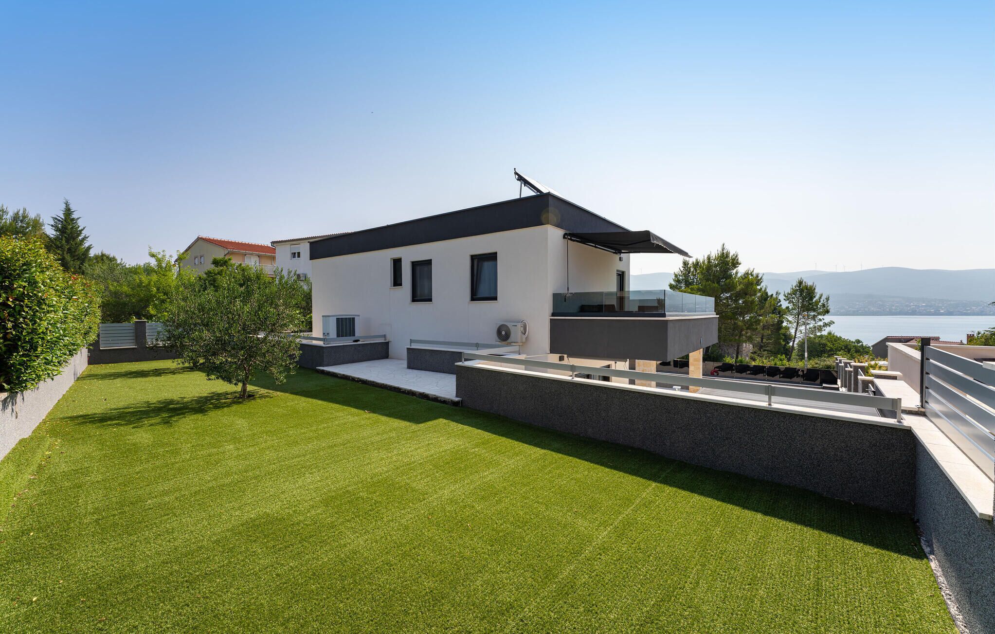 A modern two-story house with a flat roof, a balcony, and a view of the sea.