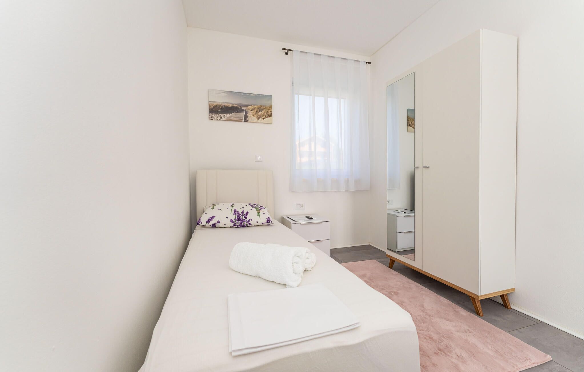 A minimalist bedroom with a single bed, a bedside table, a mirror, and a wardrobe.