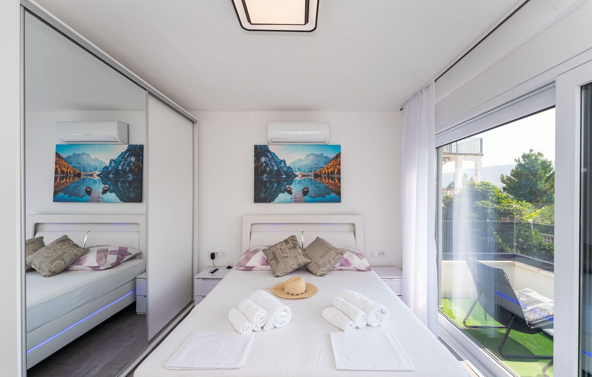 A modern hotel room with a large bed, two side-by-side beds, artwork on the walls, and a balcony with a view.