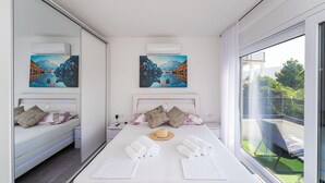 A modern hotel room with a large bed, two side-by-side beds, artwork on the walls, and a balcony with a view. - Nice home in Pridraga (Pridraga)