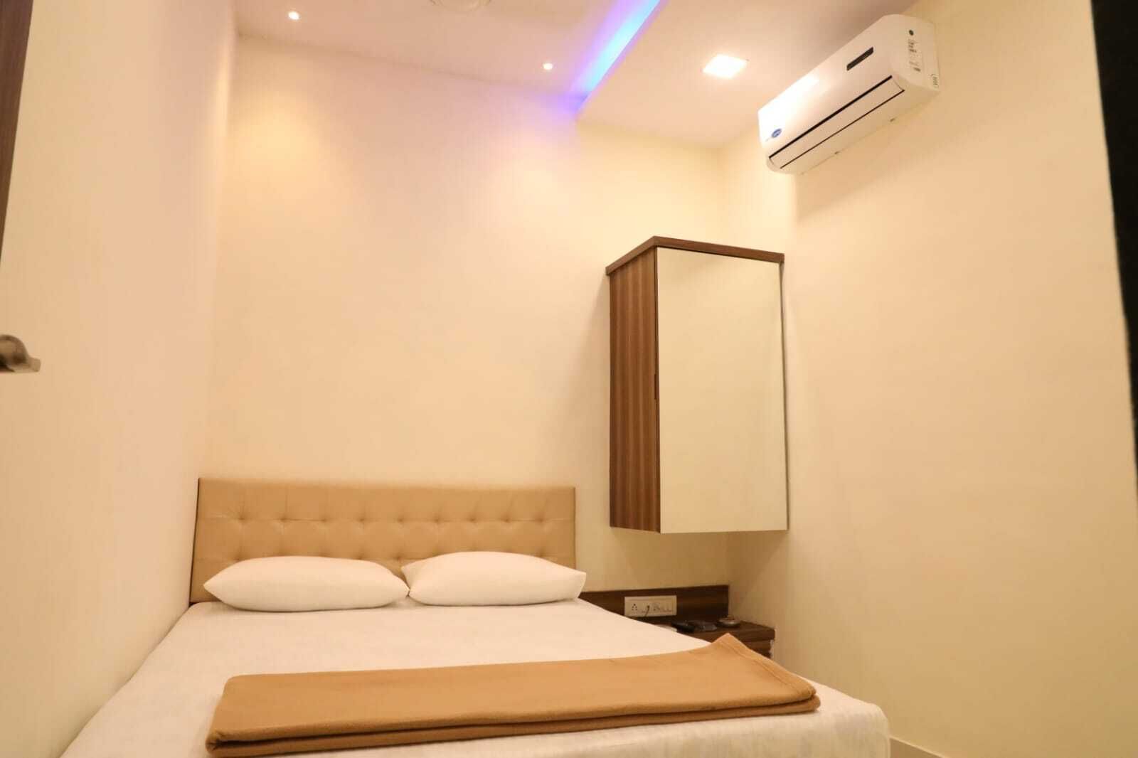 A hotel room with a bed, a nightstand, a mirror, and an air conditioning unit.