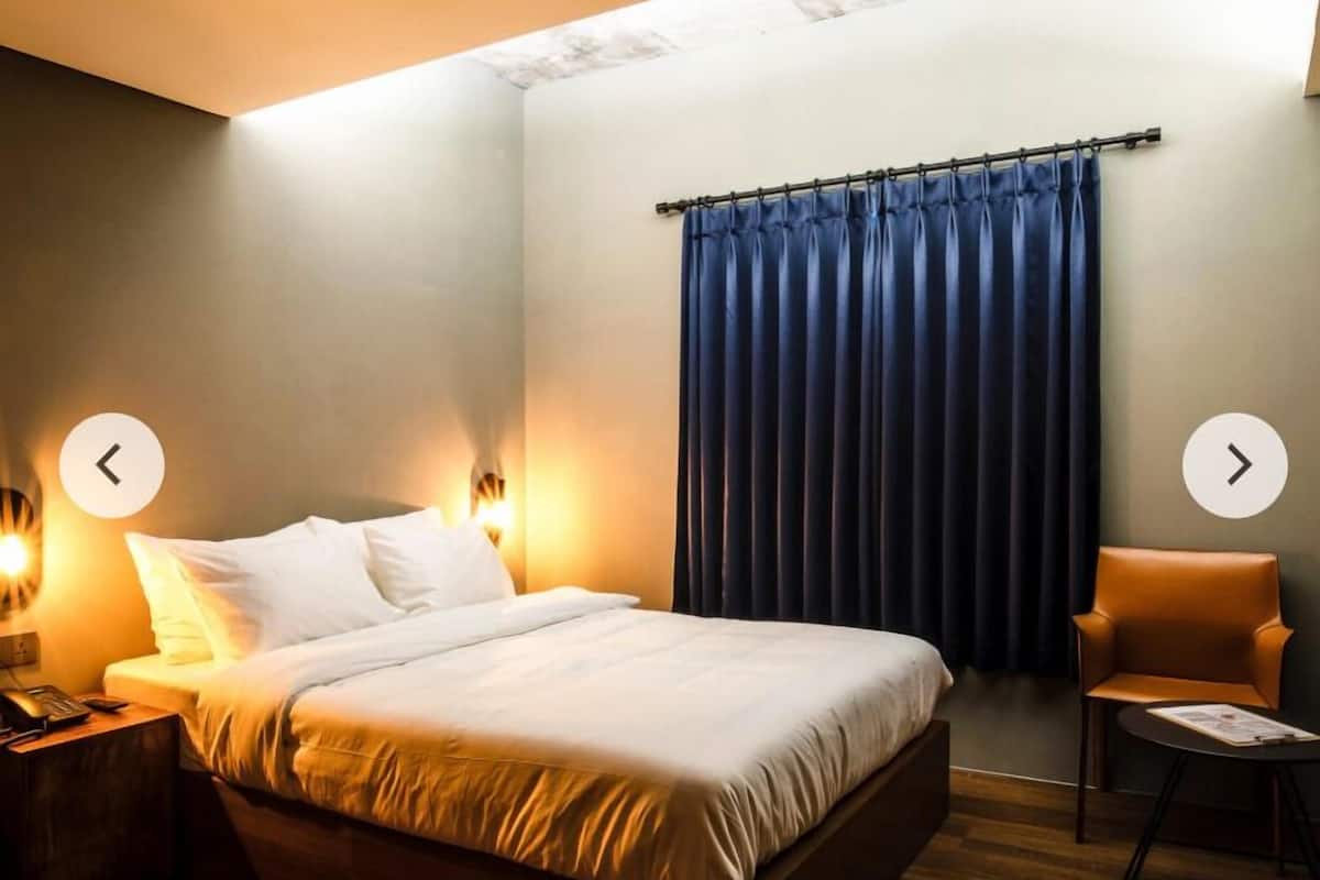 A modern hotel room with a large bed, bedside tables, a chair, and a window with curtains.