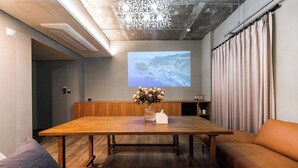 Ein Konferenzraum mit einem Holztisch, einer Projektionsleinwand, einer Vase mit Blumen und einem Sofa.