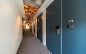 Pasillo de hotel con una puerta azul marcada '407', un accesorio de iluminación moderno y un timbre.