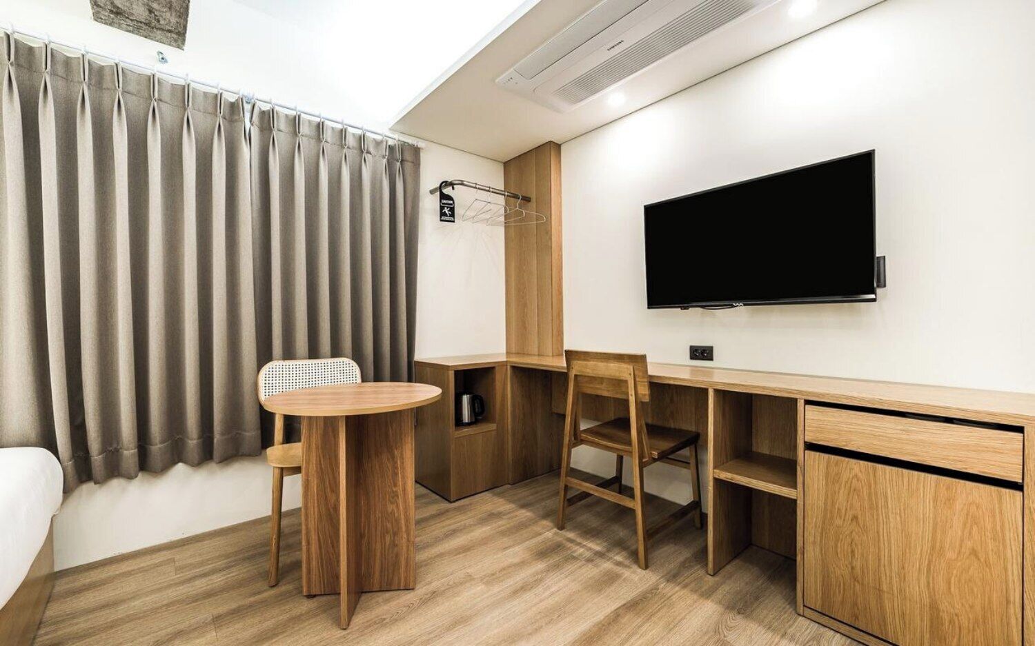 Una habitación de hotel con cama, un escritorio de madera, televisor y ventana con cortinas.