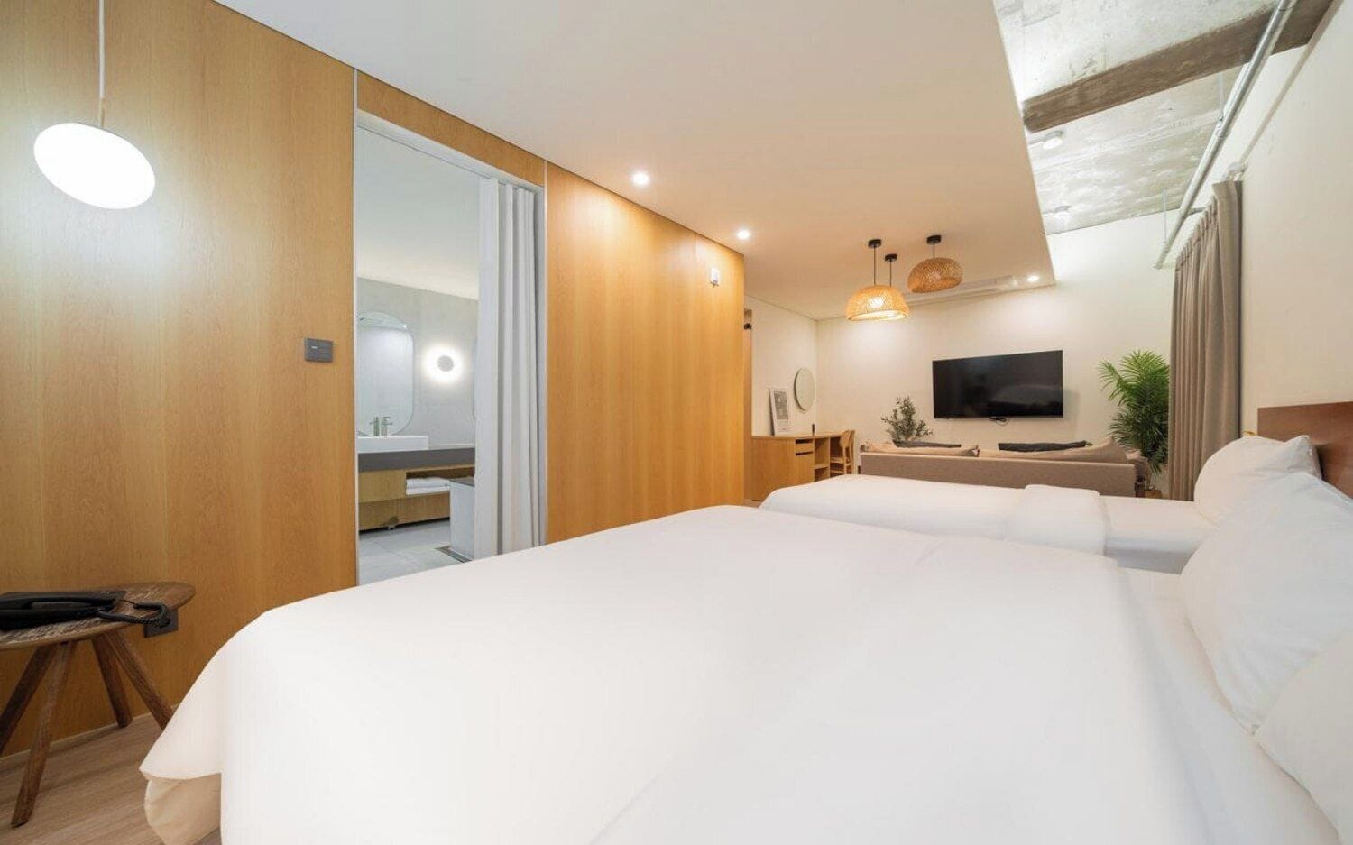 Habitación de hotel con dos camas, televisión, escritorio y baño visible a través de una puerta abierta.