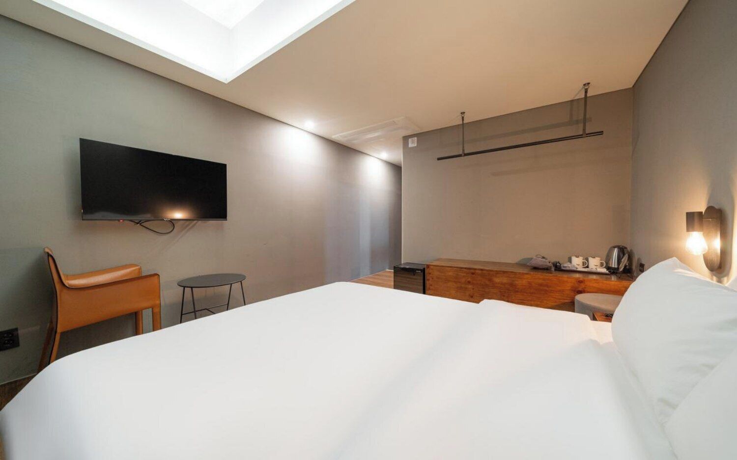A modern hotel room with a bed, a desk, a chair, a TV mounted on the wall, and a skylight.