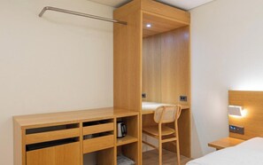 Pieni makuuhuone, jossa on puinen sänky, työpöytä ja tuoli. Huoneessa on yöpöytä, jossa on lamppu, sekä pieni hylly, jossa on vedenkeitin.