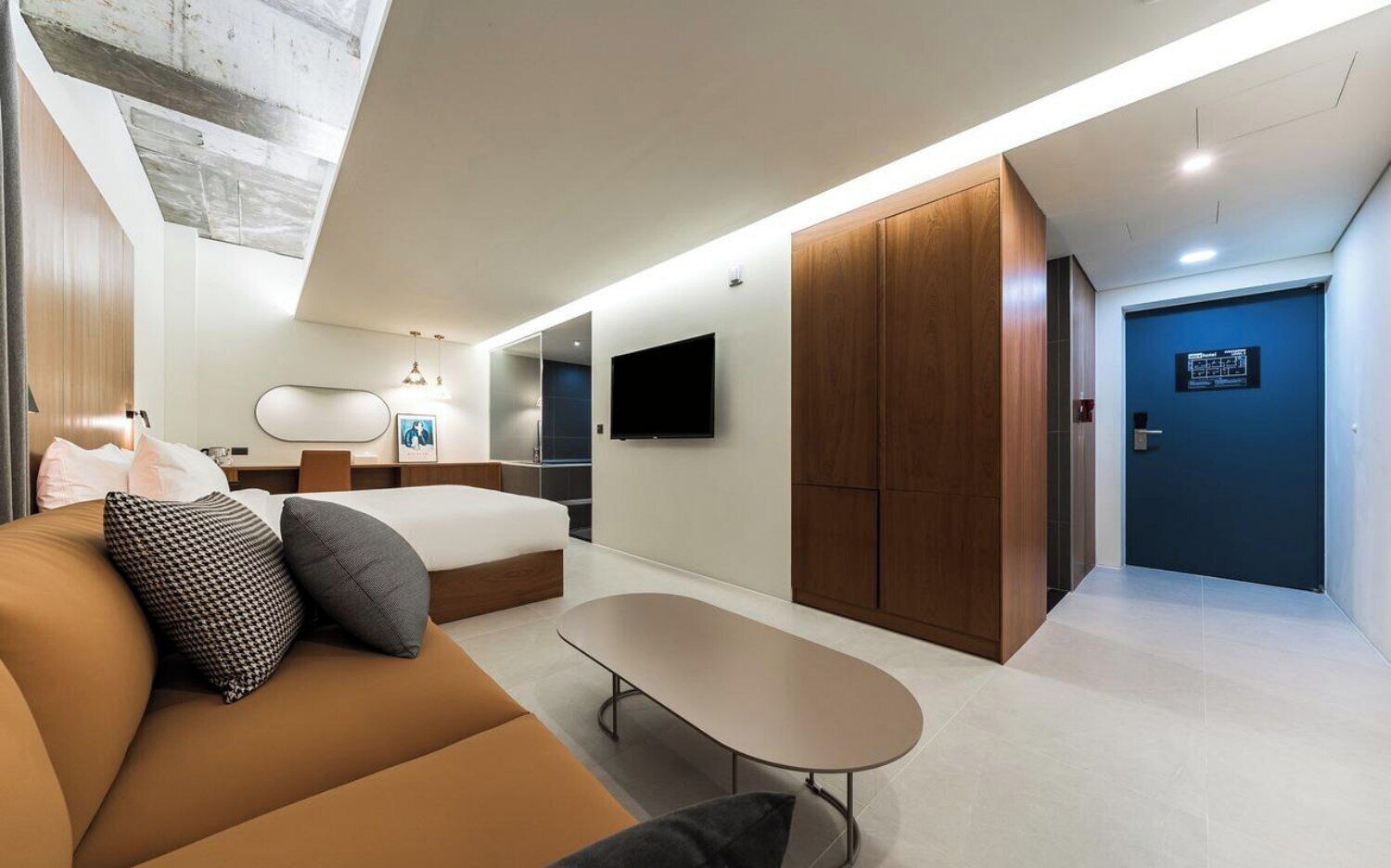 A modern hotel room with a bed, sofa, TV, wardrobe, and a small table.