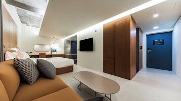 A modern hotel room with a bed, sofa, TV, wardrobe, and a small table.