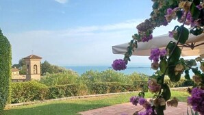Un jardín con vistas al mar, una pequeña torre y flores moradas.