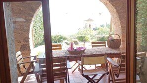Un espacio de comedor al aire libre con un arco de piedra, mobiliario de madera y vistas a un edificio distante.