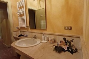 Ein Badezimmer mit Waschbecken, Spiegel, Handtuchhalter und einer kleinen Vase mit Blumen.