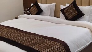 Een hotelkamer met een bed, witte beddengoed, een bruine gebreide plaid en een hoofdbord.