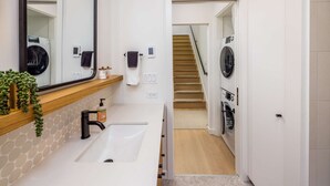 A modern bathroom with a sink, mirror, towel rack, and a staircase leading to a laundry area with multiple washing machines. - Secret Hideaway - New Custom Built Home (Seattle)