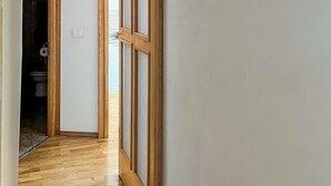 Un estrecho pasillo con suelo de madera que conduce a una habitación donde se ve un inodoro al fondo.