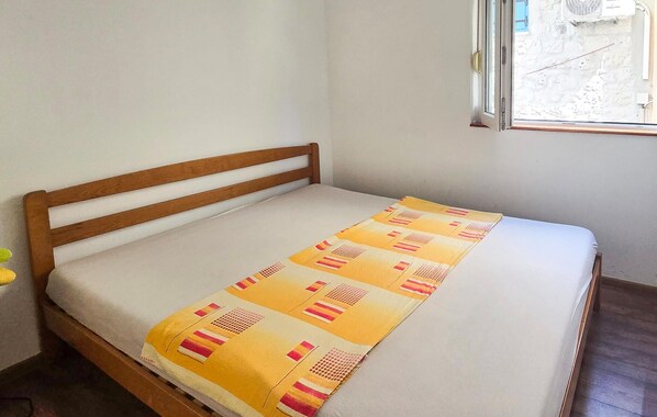 Un lit simple avec une tête de lit en bois, dans une pièce dont un mur est peint en blanc et qui possède une fenêtre.