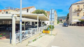 A street view with outdoor seating at a restaurant, a yellow planter, and a car parked on the road.