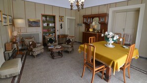 Un coin repas avec une nappe jaune, des chaises en bois, un lustre et une bibliothèque.
