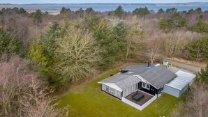 A modern house with a large deck, surrounded by dense trees and a view of the sea. - "Iris" - 200m to the fjord by Interhome (Thyholm)