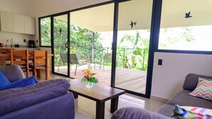 A modern living room with a sofa, a coffee table with a flower vase, and a balcony with chairs and a view of greenery. - Villa Bruno - Terrace - Jungle - Birdwatching (Puerto Jiménez)