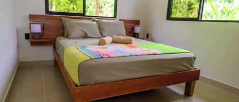Un letto con struttura in legno, biancheria beige e una coperta patchwork colorata. Due lampade da parete sono poste ai lati del letto.