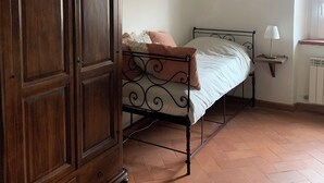 A bedroom with a wooden wardrobe, a metal bed frame, a bedside table with a lamp, and a radiator. - Detached house in the middle of the Tuscan chestnut forest (Arcidosso)