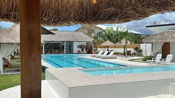 Un espace piscine doté d’une structure avec toit de chaume, de chaises longues et offrant une vue dégagée sur la piscine.