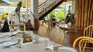 A restaurant with white tables, wicker chairs, and a staircase leading to an outdoor area.