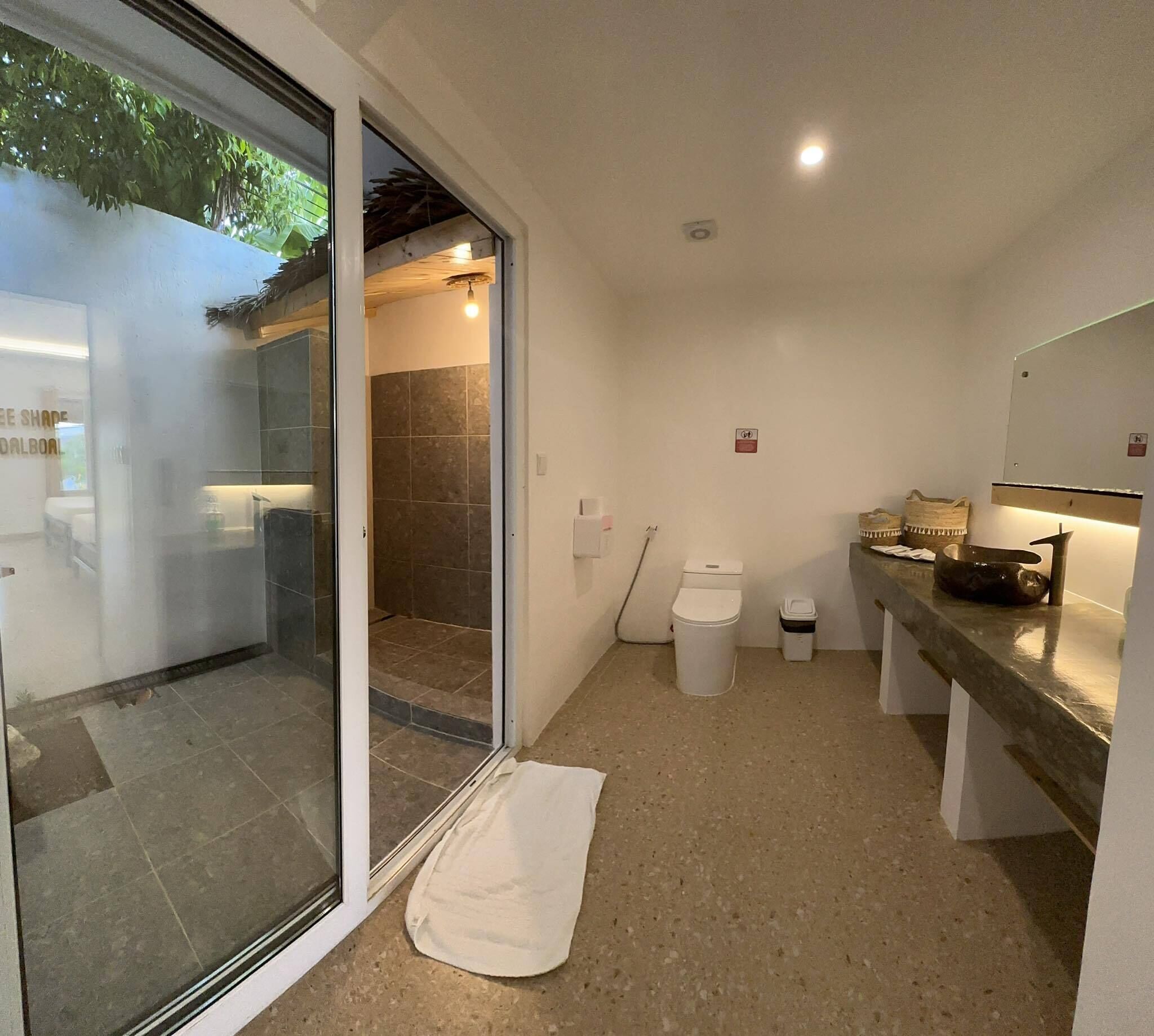 Un baño con puerta de cristal, zona de ducha, inodoro y un banco.