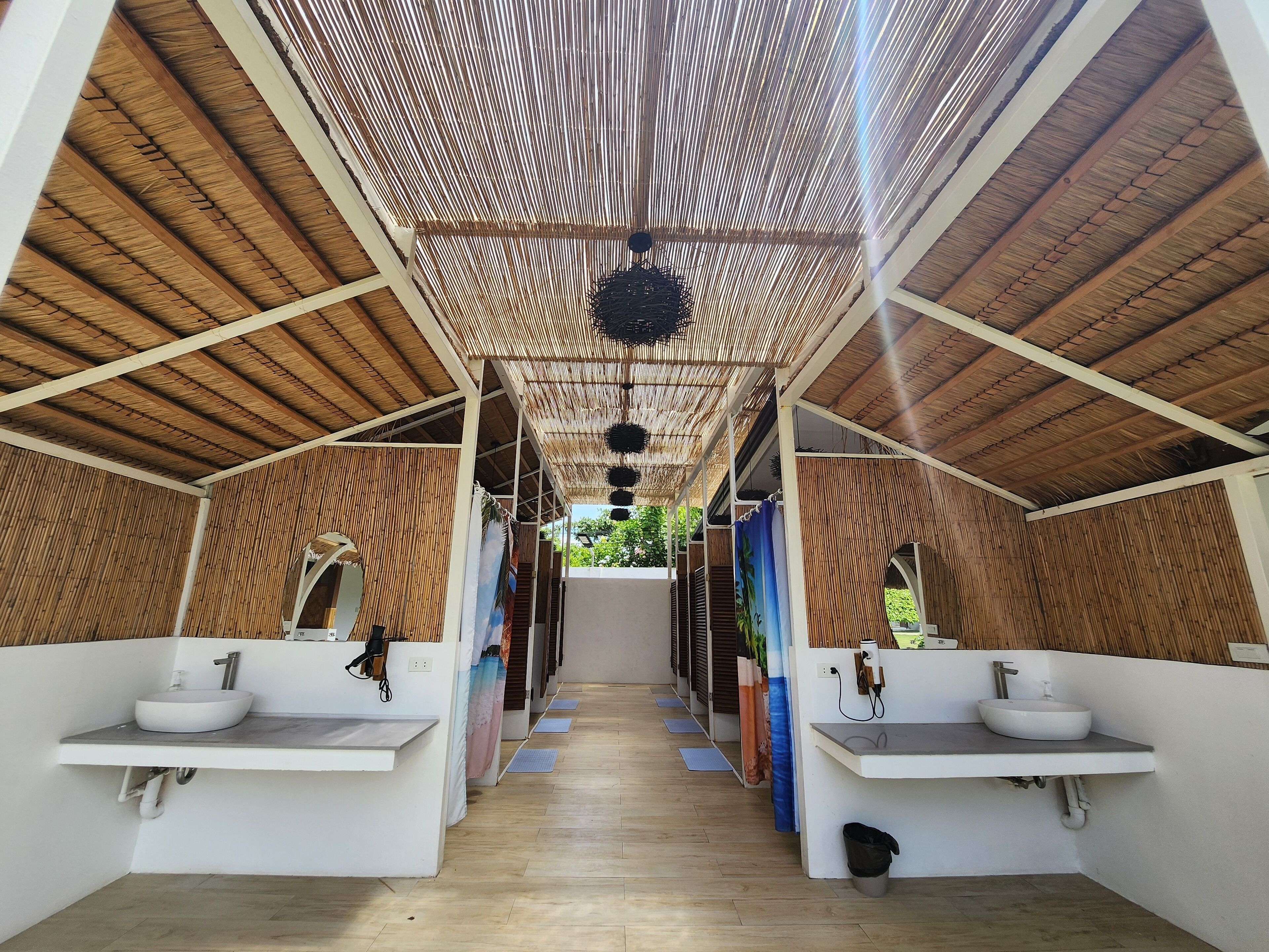 A covered outdoor bathroom with two sinks, wooden ceiling, and a view of greenery.