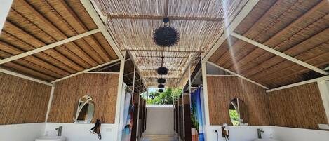 A covered outdoor bathroom with two sinks, wooden ceiling, and a view of greenery.