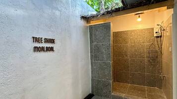 Un baño moderno con ducha, un lavamanos pequeño y un inodoro de pared.