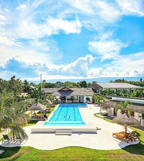 A swimming pool surrounded by thatched-roof structures, a grassy area, and a view of distant mountains. - Treeshade Resort & Spa Moalboal (Moalboal)