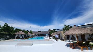 A resort with a swimming pool, thatched-roof huts, and lounge chairs.
