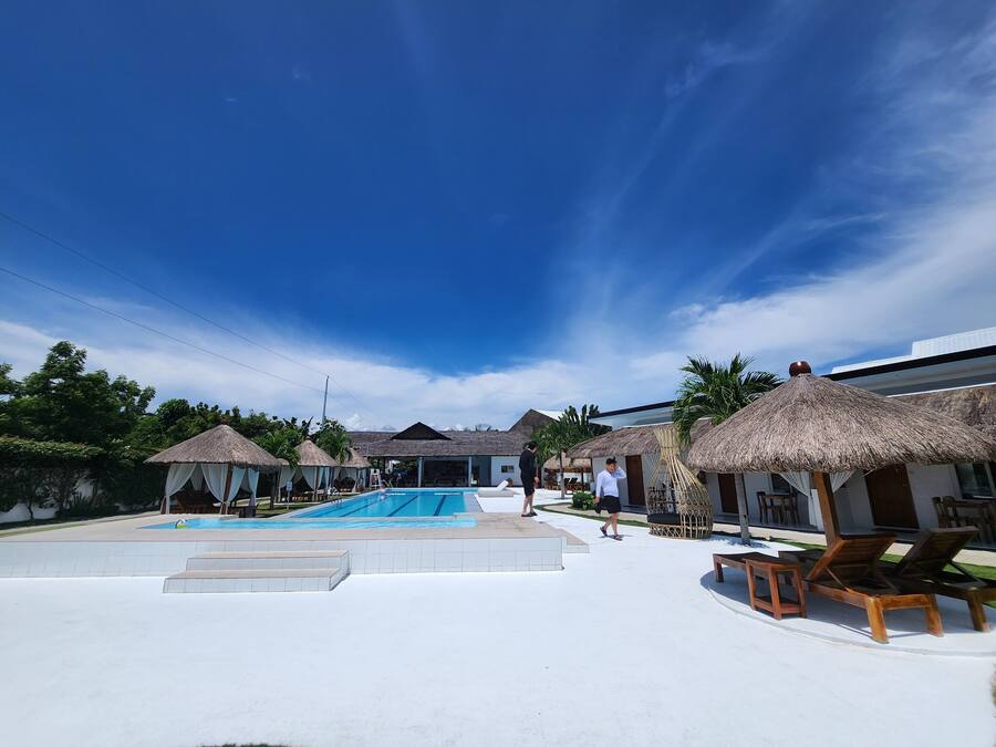 A resort with a swimming pool, thatched-roof huts, and lounge chairs.