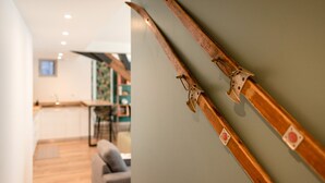 A room with a wooden ski rack against a wall, a kitchen area in the background, and a sofa in the foreground. - Charming apartment 5P (Cauterets)