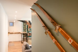 Ein Zimmer mit einem Holz-Ski-Ständer an der Wand, ein Küchenbereich im Hintergrund und ein Sofa im Vordergrund.