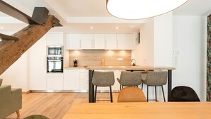 A modern kitchen with white cabinets, a wooden island, and a dining area with a table and chairs. - Charming apartment 5P (Cauterets)