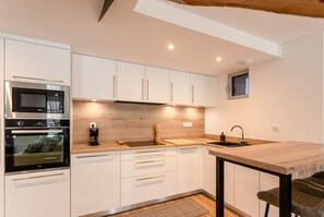 A modern kitchen with white cabinetry, a built-in oven, a coffee machine, and a wooden countertop. - Charming apartment 5P (Cauterets)