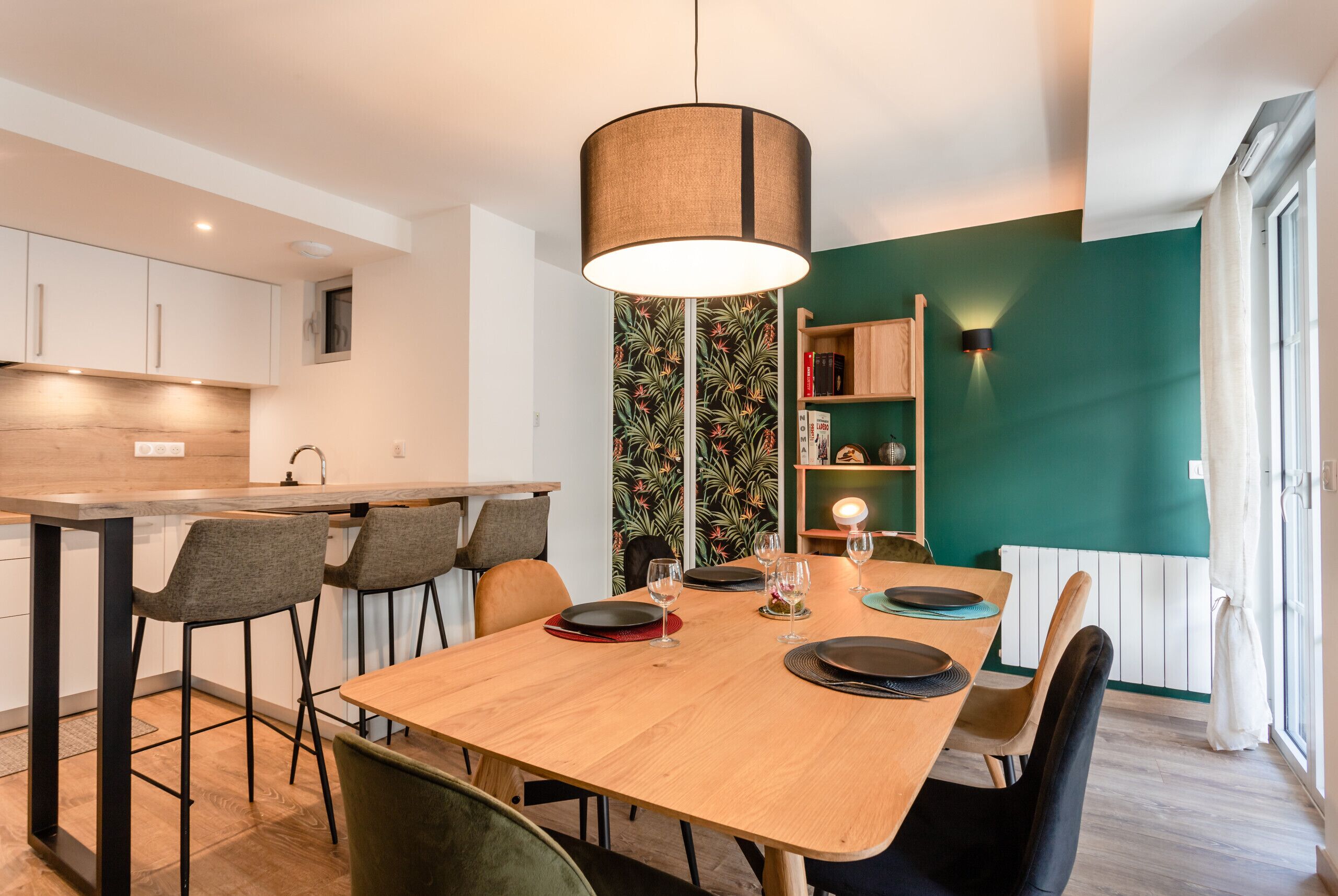 A modern kitchen with a wooden table set for dining, a hanging light fixture, and a green accent wall.