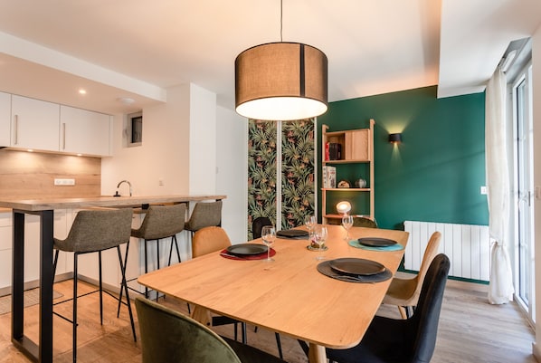 Eine moderne Küche mit Holztisch, gedecktem Esstisch, einer Pendelleuchte und einer grünen Akzentwand.