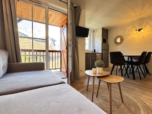 Una habitación con dos camas, una mesa de comedor con sillas, una pequeña cocina y un televisor fijado a la pared.